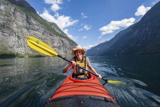 Kayak trip on the Geirangerfjord, young man paddling in red kayak, atmospheric fjord landscape,