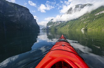 Kayak trip on the Geirangerfjord, tip of a red kayak in the fjord with reflection, atmospheric