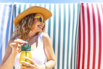 Young woman with straw hat and sunglasses enjoying a refreshing pineapple cocktail on a beach with