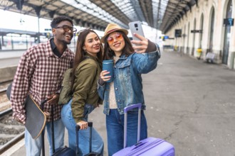 Three happy young tourists taking a selfie with a smartphone while waiting for their train, ready