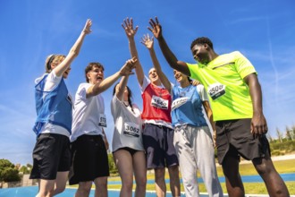 Group of young athletes celebrating their victory on a running track, raising hands together in a
