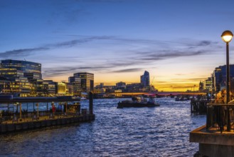 Tugboats sailing on thames during sunset with london's illuminated skyline reflecting on the water