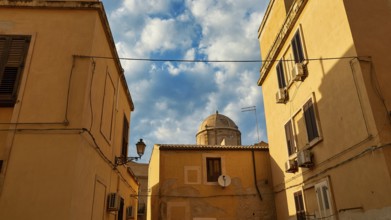 Narrowed view of a dome, framed by yellow houses and cables, with partly cloudy sky, Ortigia