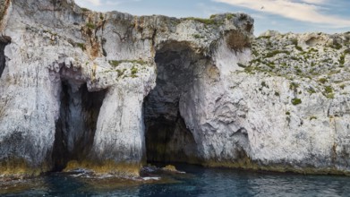 Rocky cave formations on the coast under a blue sky, boat trip around the island of Ortigia, Isola