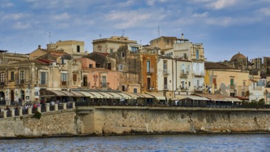 Coastal view with a mix of old buildings and modern terraces along the waterfront, boat trip around