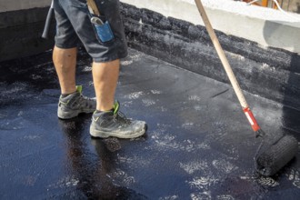 Flat roof waterproofing: Roofer applying the bitumen primer
