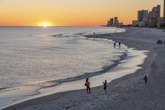 People walking and playing on the beach as the sun sets over the Gulf of Mexico at Gulf Shores,