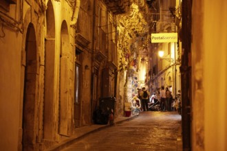 Atmospheric nocturnal alley with warm light and people in front of historic buildings under a