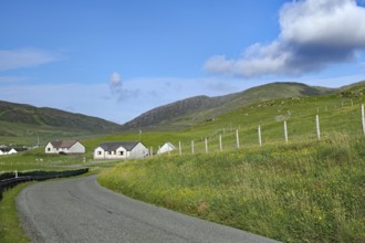 Winding country road leads through a rural area with meadows and houses under a blue sky, Barra,