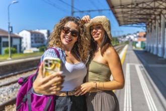 Two female tourists taking a selfie with smartphone on a train station platform during summer