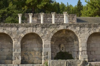 Ancient ruins with arches and columns, surrounded by forest and vegetation, retaining wall with