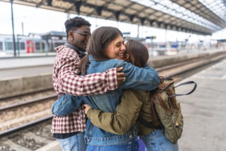 Three happy students hugging each other at the train station, excited for their journey or happy to