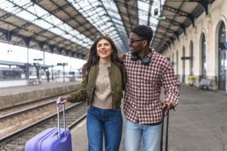 Young multi ethnic couple walking together with luggage at a train station platform, enjoying their
