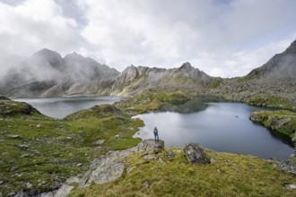 Mountaineer on a rock in front of mountain lakes Wangenitzsee and Kreuzsee, cloudy mountain peaks