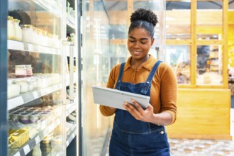 Young supermarket employee using digital tablet checking inventory of dairy products inside of a