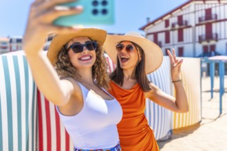 Two cheerful women wearing sun hats and sunglasses, capturing a fun selfie on a sunny beach,