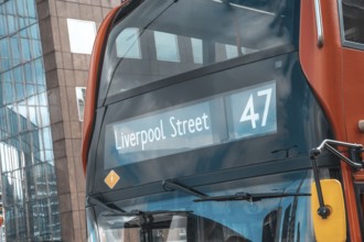 Red double decker bus number 47 showing liverpool street destination, reflecting modern buildings