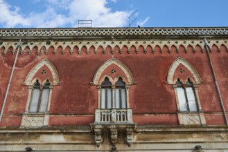 Red façade of a building with Gothic windows and decorative details, Ortigia Island, Isola di