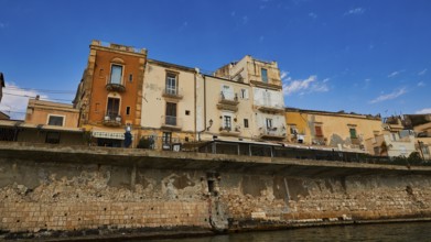 Houses with different facades on a stone coastal wall under a sunny sky, boat trip around the