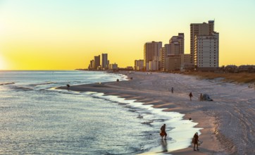 People walking and playing on the beach as the sun sets over the Gulf of Mexico at Gulf Shores,