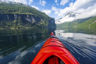 Kayak trip on the Geirangerfjord, tip of a red kayak in the fjord with reflection, atmospheric