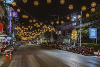 Scooters and motorcycles under lighted spheres strung across downtown street in Chiang Rai,