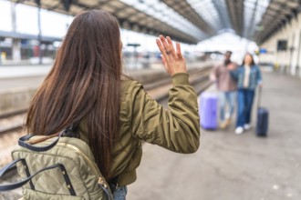 Young woman waving goodbye to friends arriving at a train station, travel and friendship concept