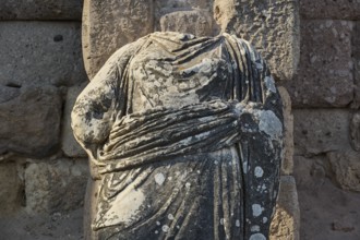 Close-up of a headless stone statue in a landscape of ruins, torso of a statue of a god, Asklipion,