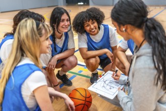 Female basketball coach drawing a play on a clipboard while explaining game strategy to her young