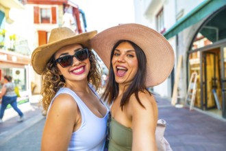 Two female tourists are taking a selfie while walking down a city street during their summer