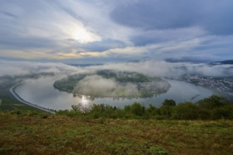 Fog-covered river landscape with rolling hills and overcast sky in calm light, summer, Rhine bend