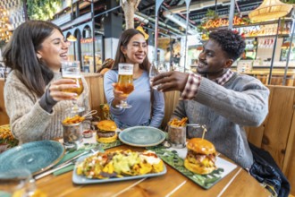 Happy multi ethnic friends toasting drinks and enjoying a delicious meal together at a lively