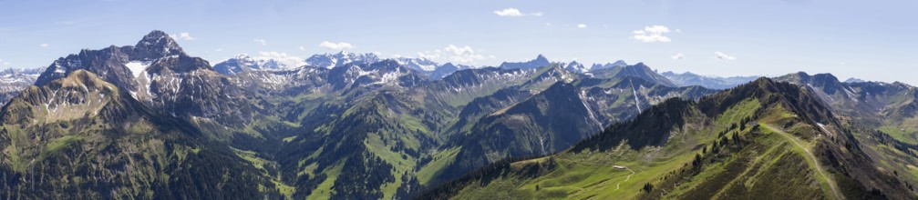 Sweeping panorama of the Alps with snow-capped mountains and green valleys under a blue sky,