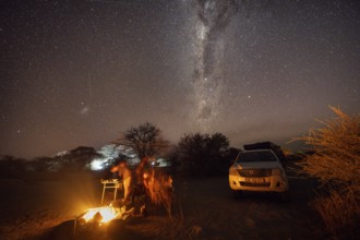 Tourists sitting around a campfire next to their off-road vehicle at night, night shot with starry