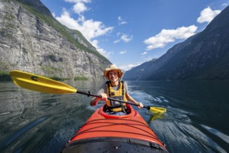 Kayak trip on the Geirangerfjord, young man paddling in red kayak, atmospheric fjord landscape,