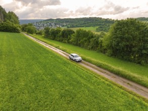 Car drives through a wide, green landscape with hills and villages on the horizon, Deer E-