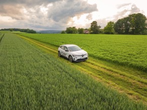A car on a path between fields under dark rain clouds in a rural area, Deer E- CarSharing, Renault