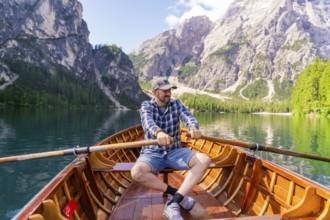 Man rowing on a mountain lake, surrounded by pine trees and steep mountain slopes, Lake Braies,