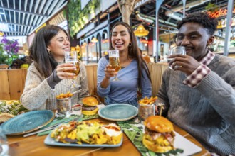 Happy multi ethnic friends are having fun together, eating burgers, nachos and fries, and drinking