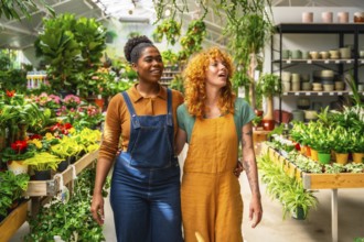 Two young women walking arm in arm through a garden center, discussing their work among vibrant