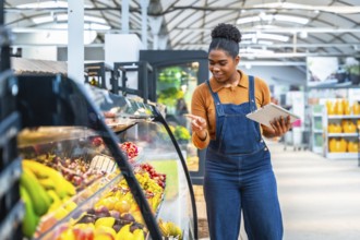 Young supermarket employee using a digital tablet and checking fresh products in a refrigerated