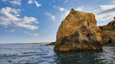 A large rock in the sea under a blue sky with white clouds, boat trip around the island of Ortigia,