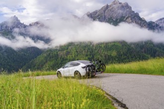 Car parked on a winding road in the impressive mountain landscape with fog and green meadows,