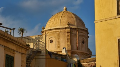 Historic dome in an old town setting with yellow buildings and palm trees, blue sky, Ortigia