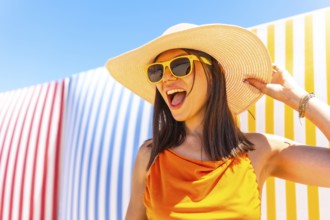 Carefree young woman wearing a straw hat and sunglasses enjoying summer vacation against a colorful
