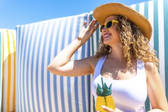 Young woman adjusting her straw hat while holding a tropical cocktail in a pineapple shaped glass