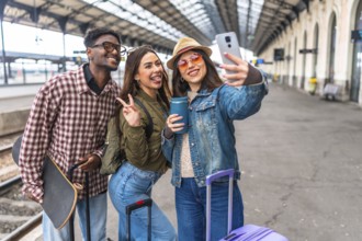 Three young tourists capturing a joyful selfie at a bustling train station, eagerly anticipating