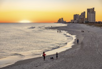 People walking and playing on the beach as the sun sets over the Gulf of Mexico at Gulf Shores,