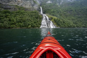 Kayak trip on the Geirangerfjord at the Freier waterfall, tip of a red kayak in the fjord,