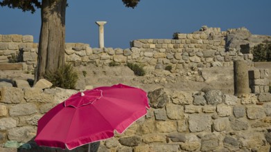 Ancient ruins with a red parasol in the foreground under a clear blue sky, Agios Stefanos Beach,